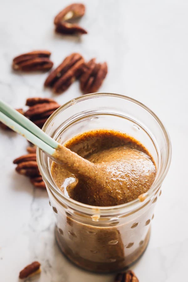 A spoon scooping out pecan butter from a glass jar.