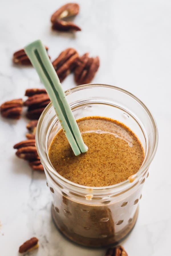 Overhead shot of pecan butter in a glass jar with a spoon. 