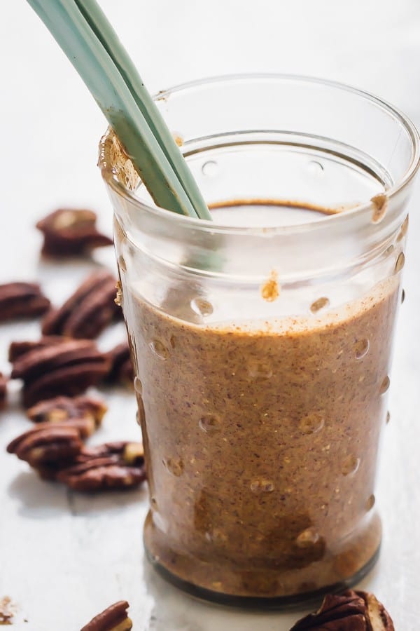 Side on shot of pecan butter in a glass jar with a spoon.