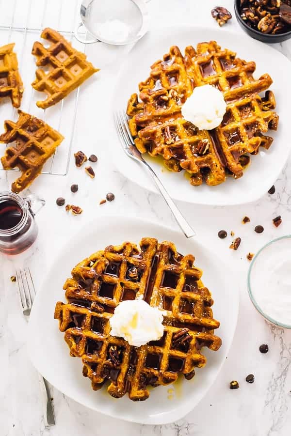 Overhead shot of two pumpkin waffles, topped with cream. 