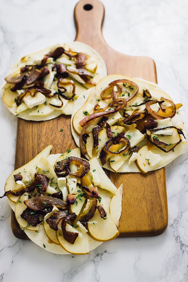Three tortillas with pear and brie slices on them.