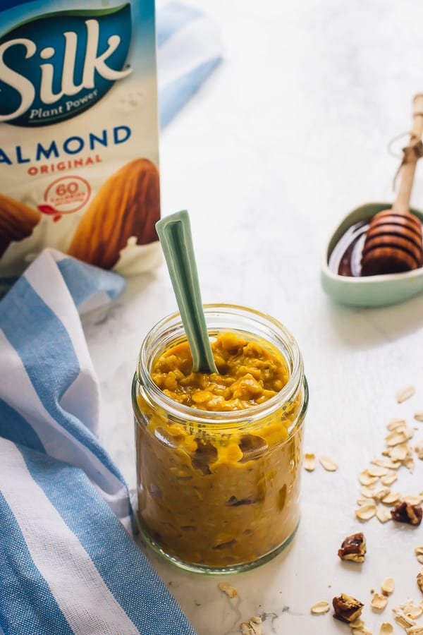 Pumpkin overnight oats in a jar with a spoon and a carton of almond milk in the background. 