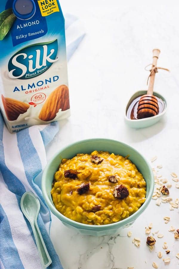 Overnight pumpkin pie oats in a blue bowl next to a carton of almond milk. 