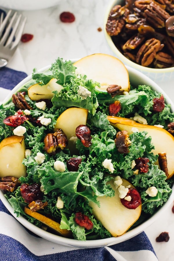 Top down shot of pear and gorgonzola salad with caramelised pecan salad in a white bowl with a bowl of pecans on the side. 