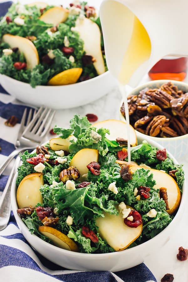 Honey dressing being poured on pear and gorgonzola salad with caramelised pecans salad in a white bowl. 