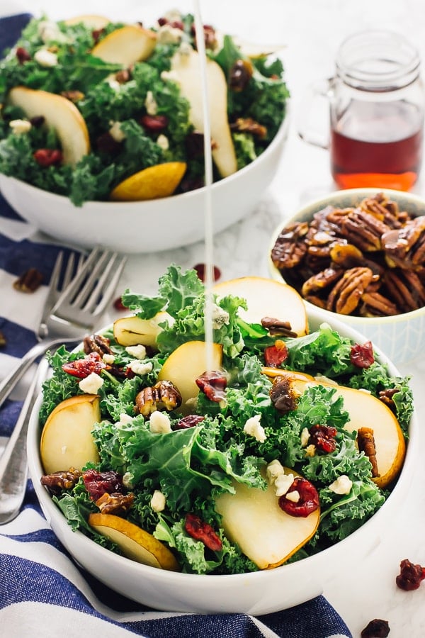 Pouring dressing on pear and gorgonzola salad with caramelised pecans salad in a white bowl. 