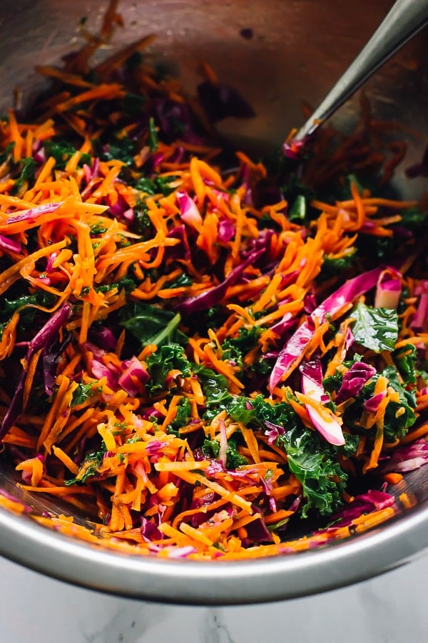Close up of kale cabbage slaw being mixed in a silver bowl.