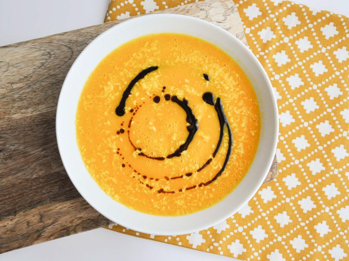 Overhead shot of vegan carrot ginger soup in a white bowl on a yellow table cloth. 