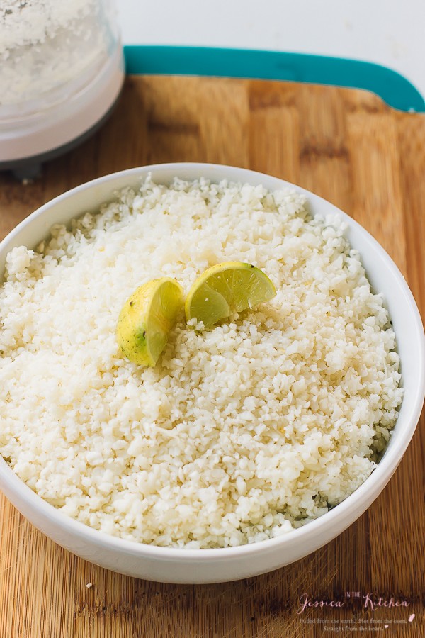 A bowl of cauliflower rice, topped with lemon wedges. 