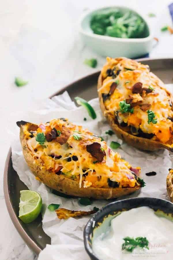 Two loaded sweet potato skins on a grey plate with lime wedges on the side. 