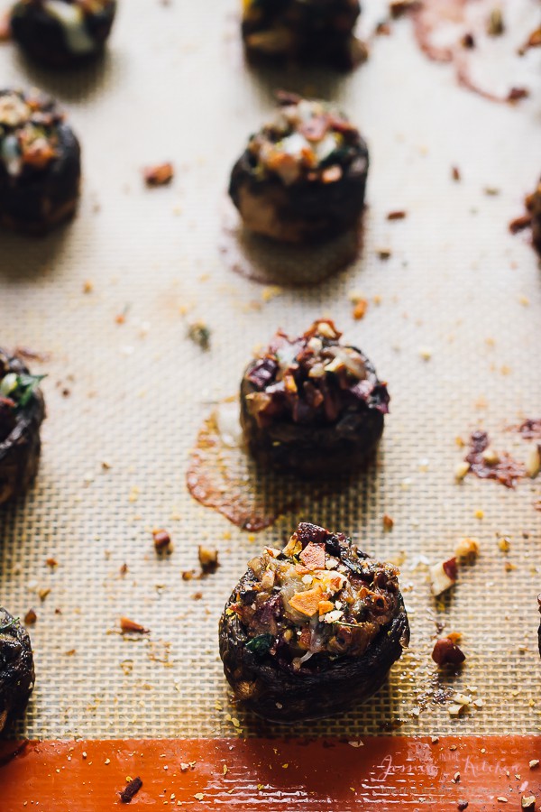 Close up of stuffed mushrooms with coconut bacon on a silpat, with pieces of nuts scattered around