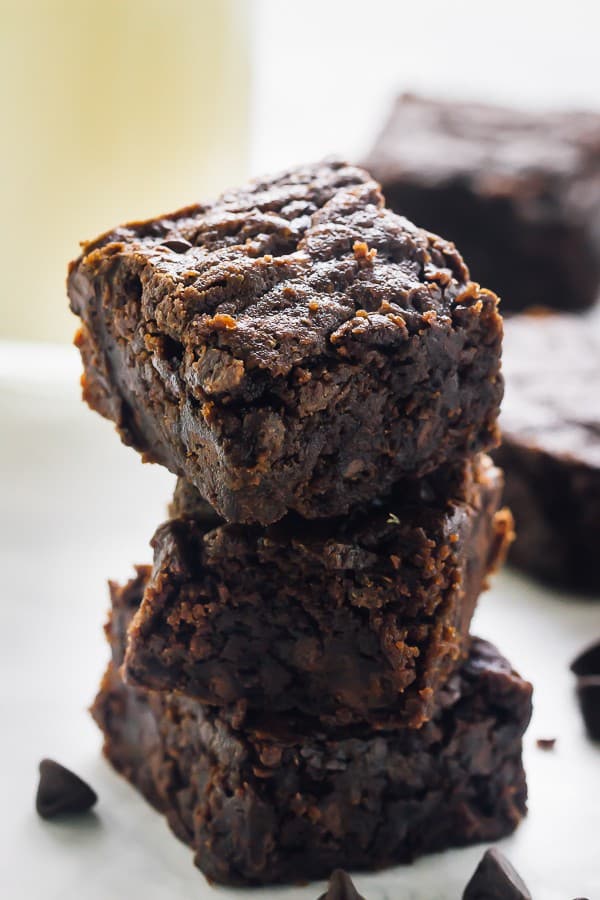 A stack of vegan brownies surrounded by chocolate chips. 