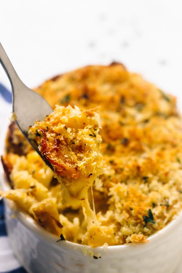 A fork pulling some mac and cheese from a white ramekin. 