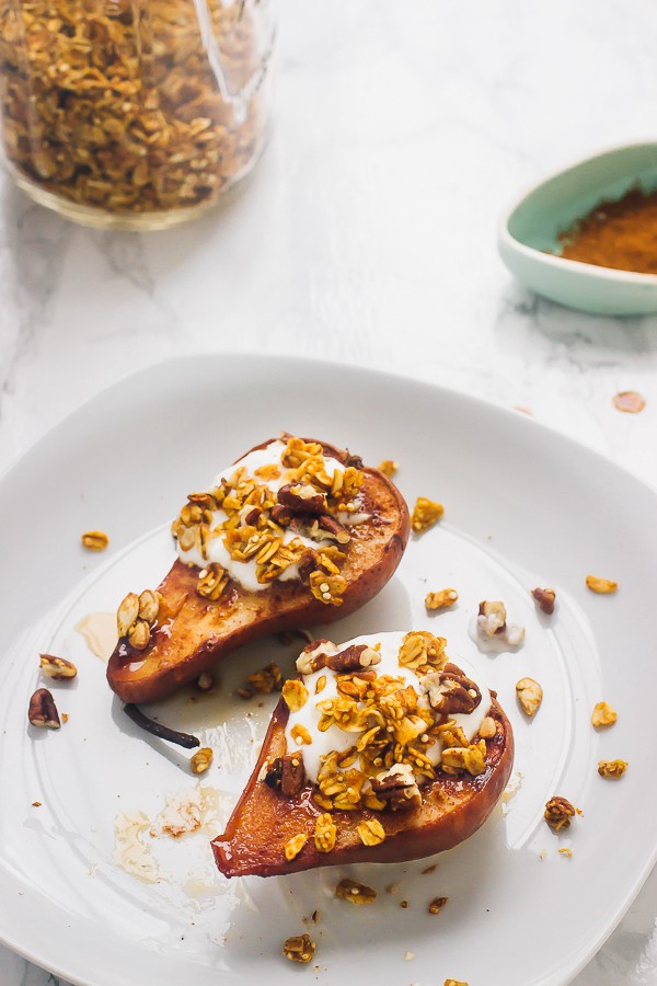 Top down shot of cinnamon baked pears topped with granola on a white plate.