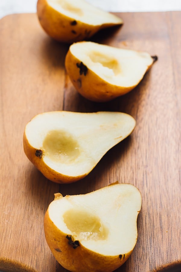 Four pear halves on a wooden chopping board. 