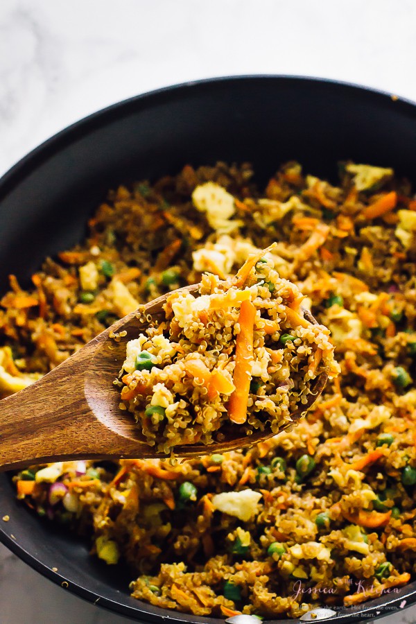  Quinoa fried rice on a wooden spoon with a skillet of quinoa rice in the background. 