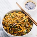 Quinoa fried rice in a white bowl with chopsticks on the side.