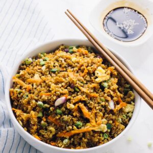 Quinoa fried rice in a white bowl with chopsticks on the side.