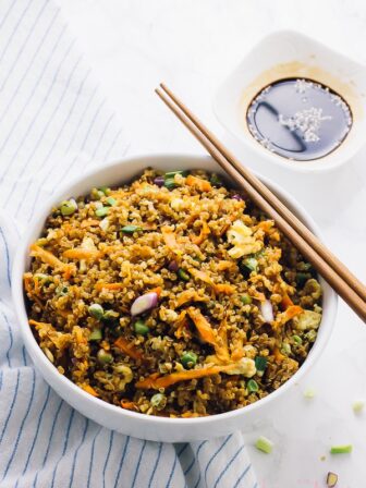 Quinoa fried rice in a white bowl with chopsticks on the side.