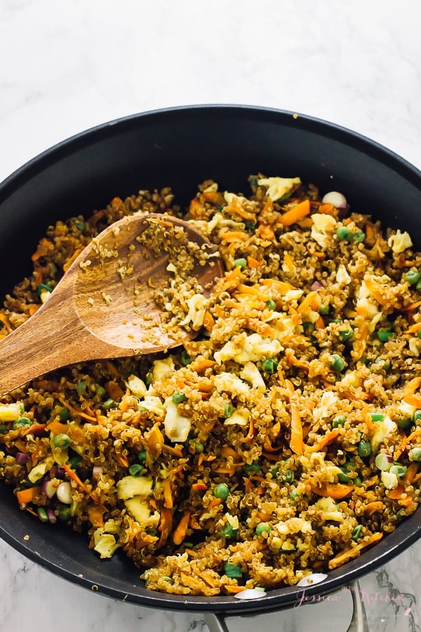 Quinoa fried rice being stirred with a wooden spoon in a black skillet. 