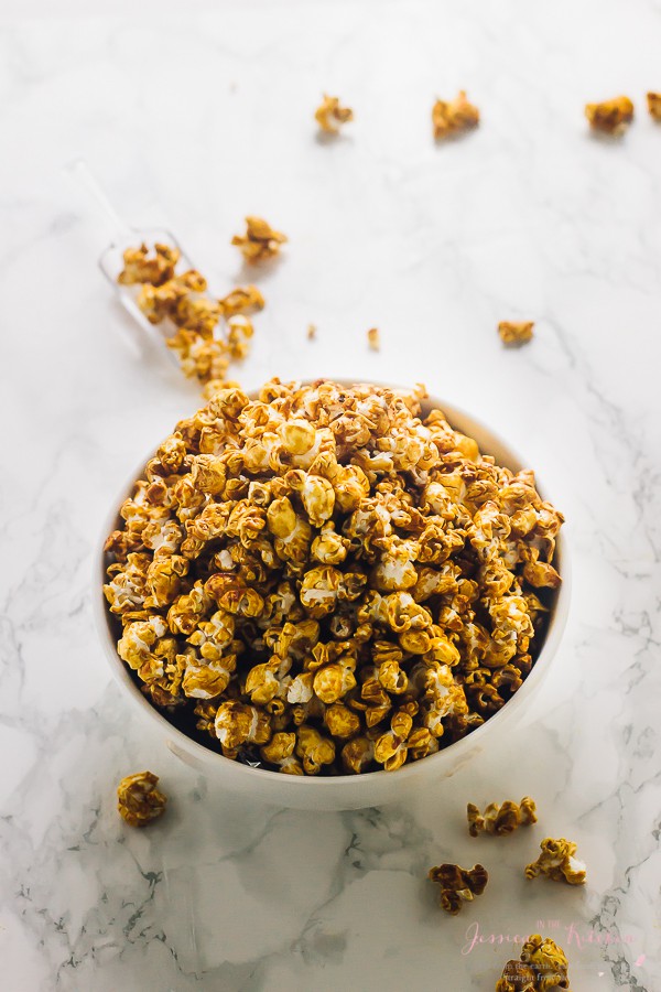 Overhead view of a bowl full of caramel popcorn on a marble surface, with pieces of caramel corn around it.