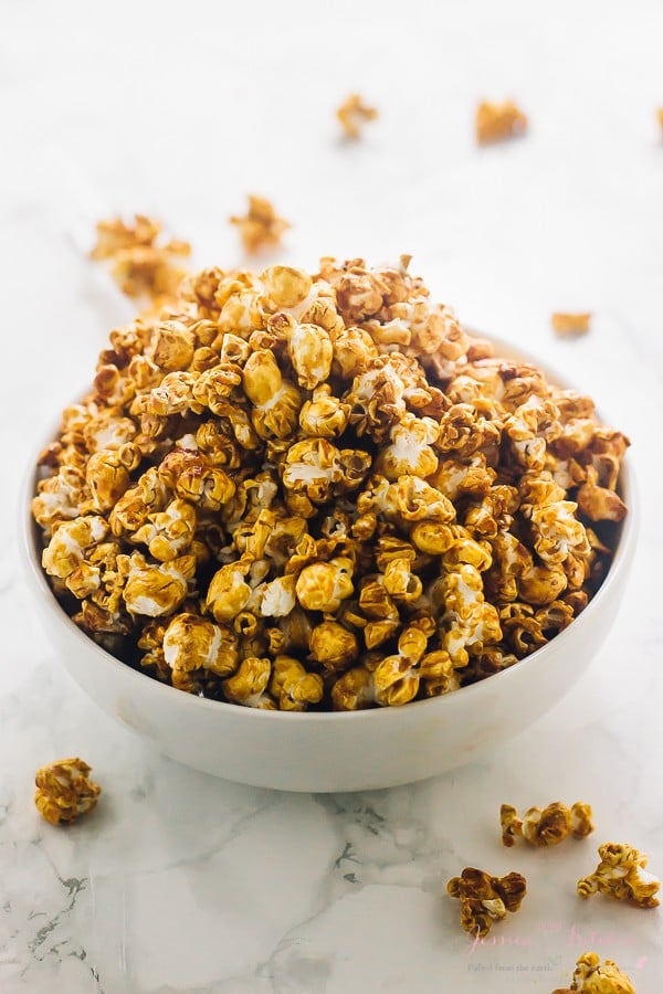 A bowl full of caramel corn with pieces on the table around it.