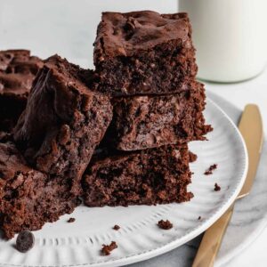Brownies stacked on a plate with knife beside it.