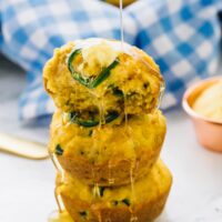 A pile of three gluten free cornbread muffins drizzled with honey.