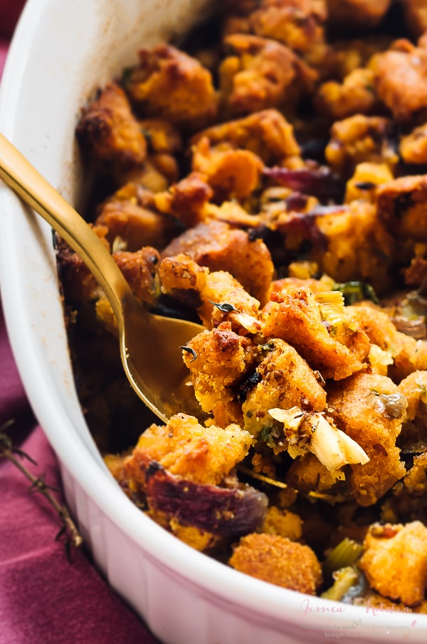 Gluten free cornbread stuffing being scooped out of a baking dish with a spoon.