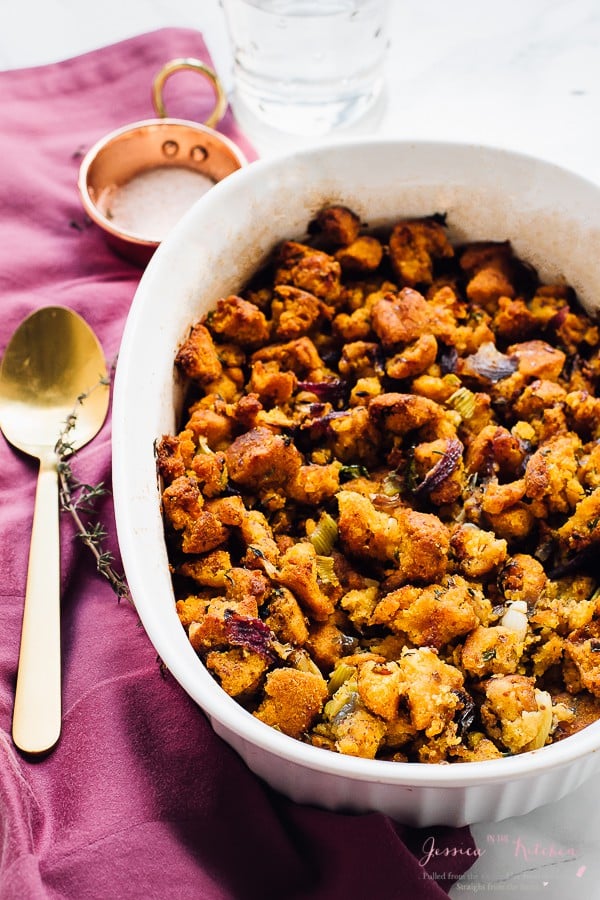 Cornbread stuffing in a white baking dish with a gold spoon on the side. 