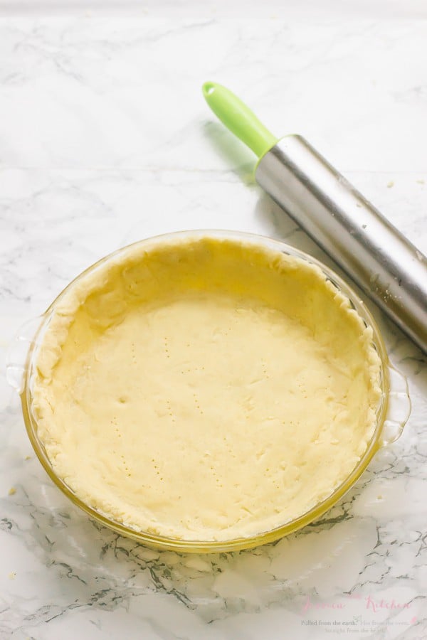 Gluten free pie crust in a glass pie dish with a rolling pin on the side. 