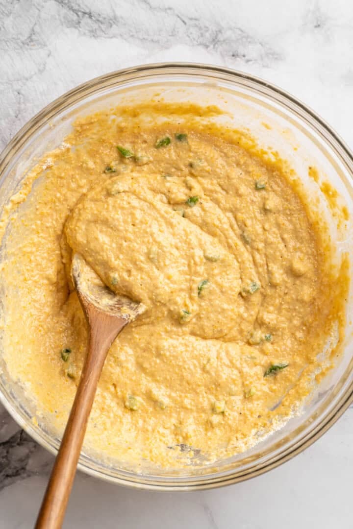 These moist vegan jalapeño cornbread muffins are easy to make and have a gluten-free option, which means everyone can enjoy them! Batter for cornbread muffins with jalapenos in bowl with wooden spoon.