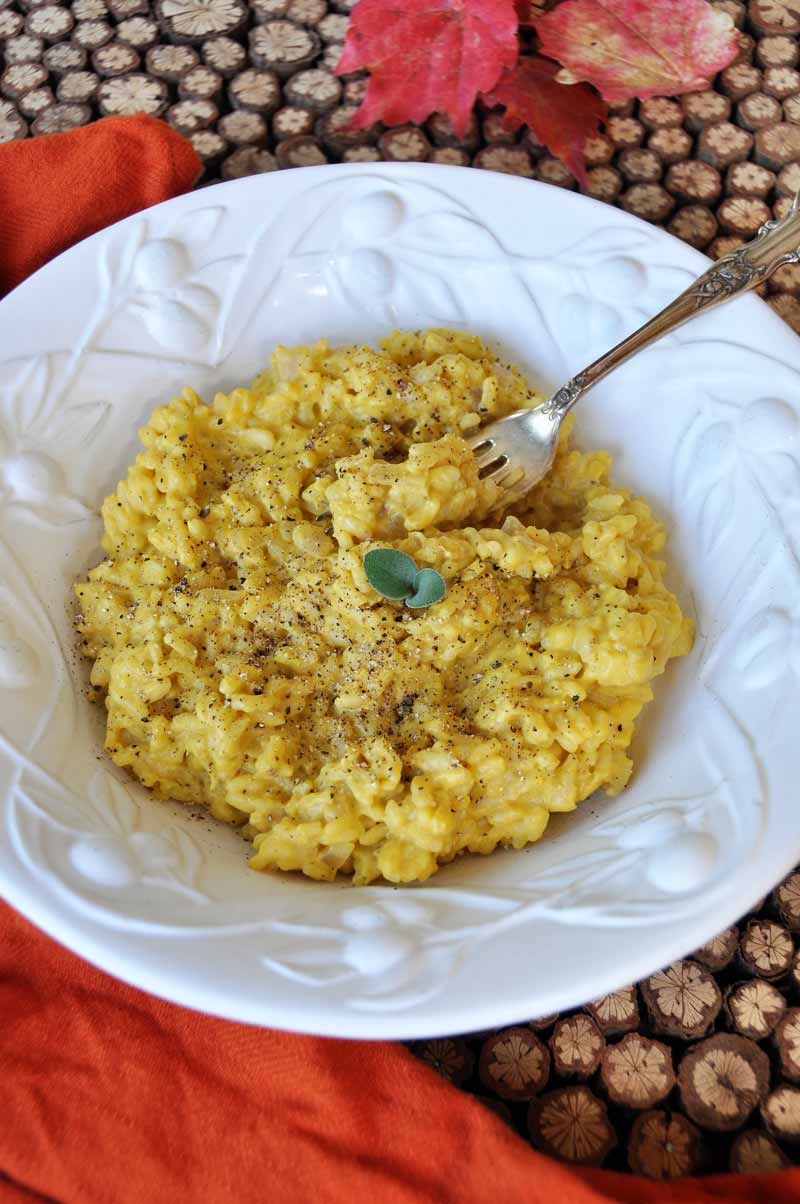 Risotto with vegan pumpkin sage cream sauce in a white bowl with a fork.