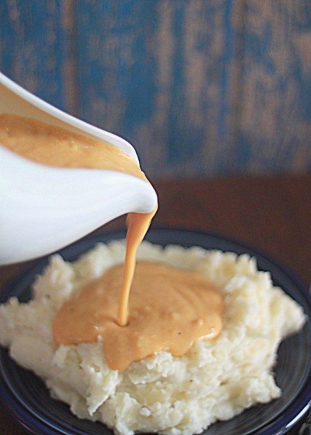 A gravy boat pouring out vegetarian onion gravy onto mashed potatoes. 