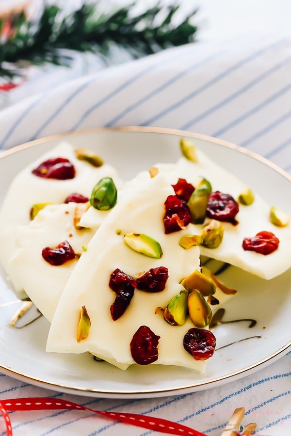 Chunks of white chocolate bark with cranberries and pistachio on a white plate. 