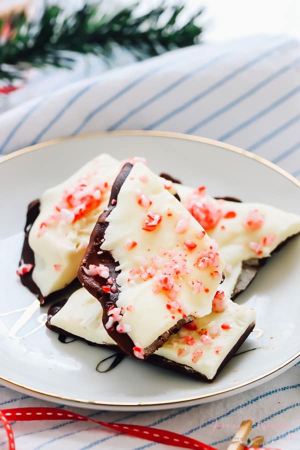 Chunks of chocolate bark with crushed candy canes on a white plate. 
