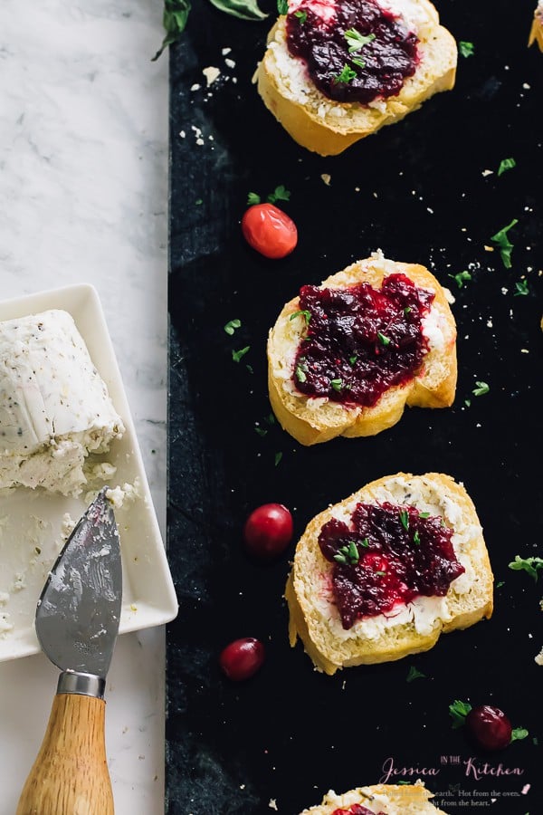 Top down shot of cranberry goat cheese crostinis on a black slate. 