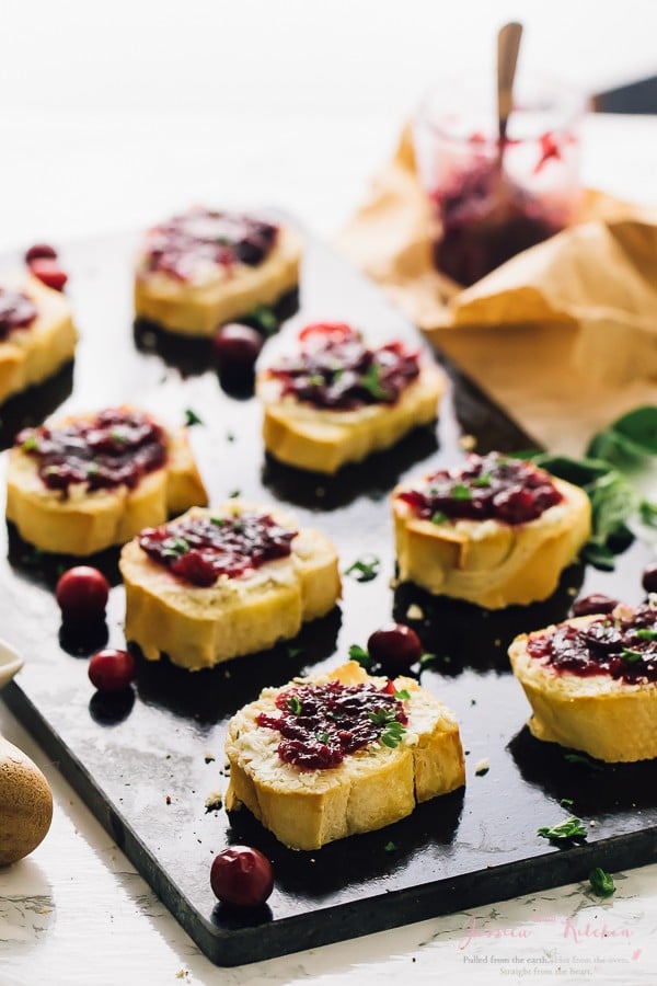 Cranberry goat cheese crostini on a black slate with cranberries. 