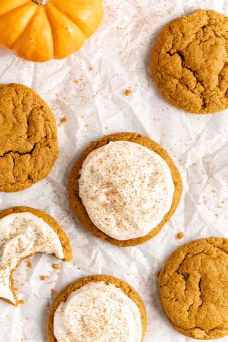 pumpkin cookies with some frosted on parchment paper close up