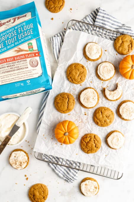 pumpkin cookies with some frosted on a wire rack