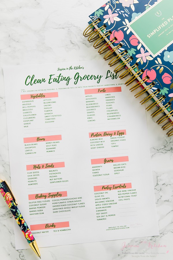 A printed clean eating grocery list on a table with a pen and notebook.