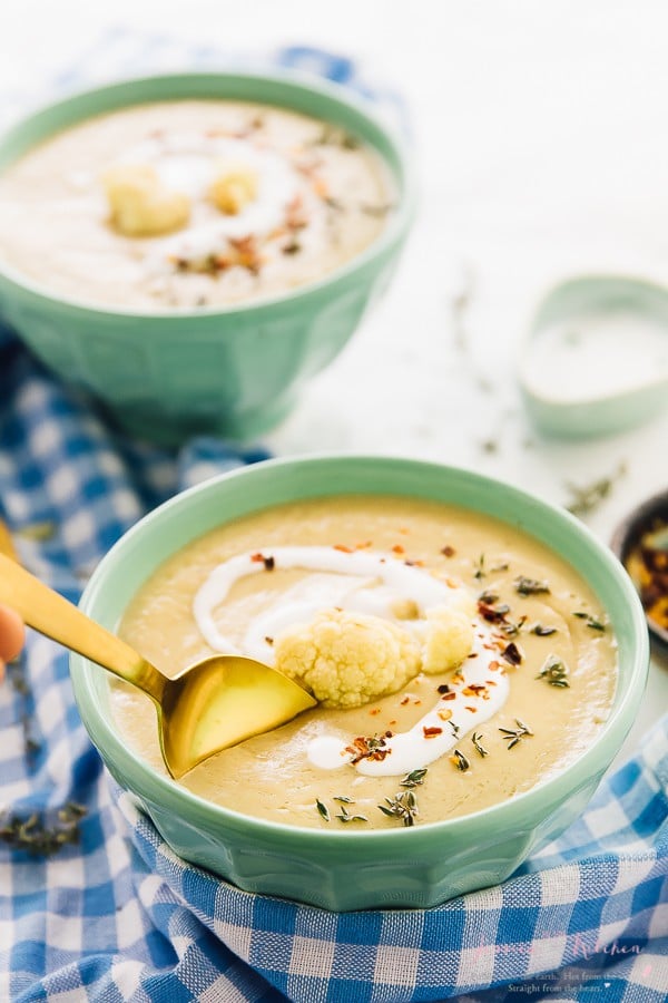 A gold spoon dipping into a blue bowl of cauliflower soup.