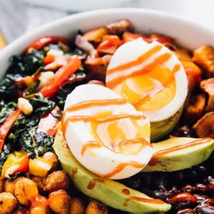 A close up of a breakfast bowl with sliced avocado and sliced egg on top.