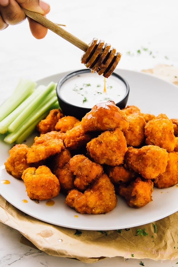 A batch of vegan cauliflower buffalo wings being drizzled with honey.