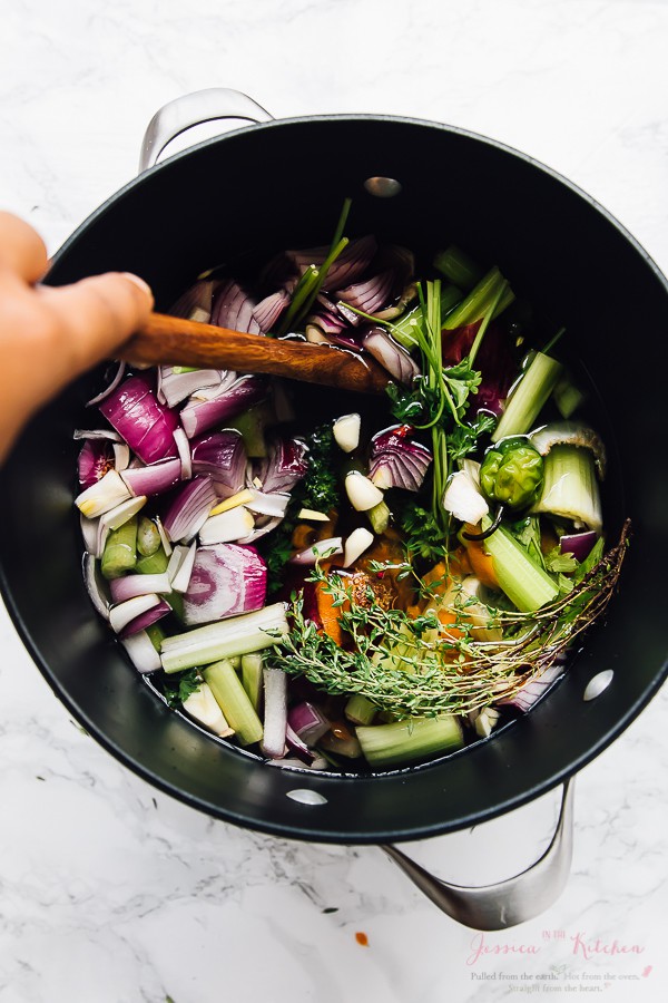 Wooden spoon stirring a vegetable broth in a black pot. 