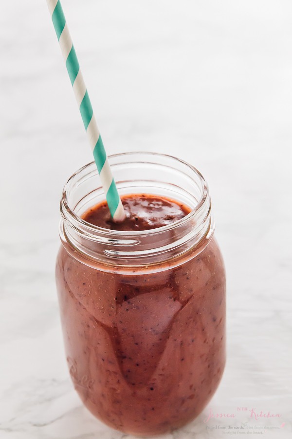 A mixed berry smoothie in a glass mason jar with a straw. 