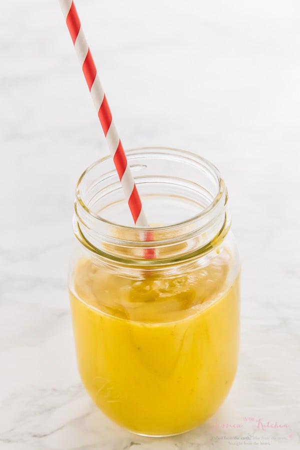 Turmeric smoothie in a glass jar with a red straw. 