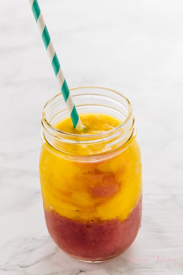 Strawberry mango smoothie in a glass mason jar with a straw. 