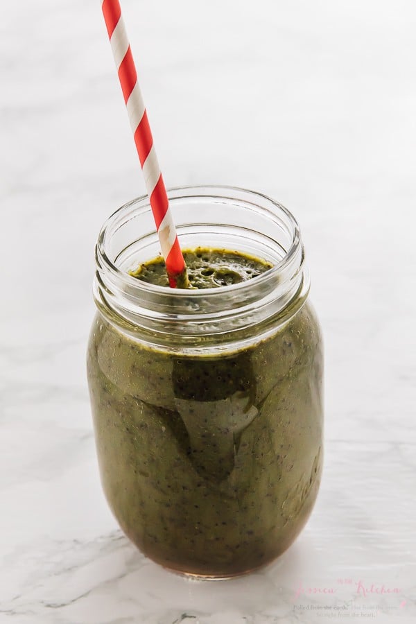 Spinach smoothie in a glass mason jar with a red straw. 
