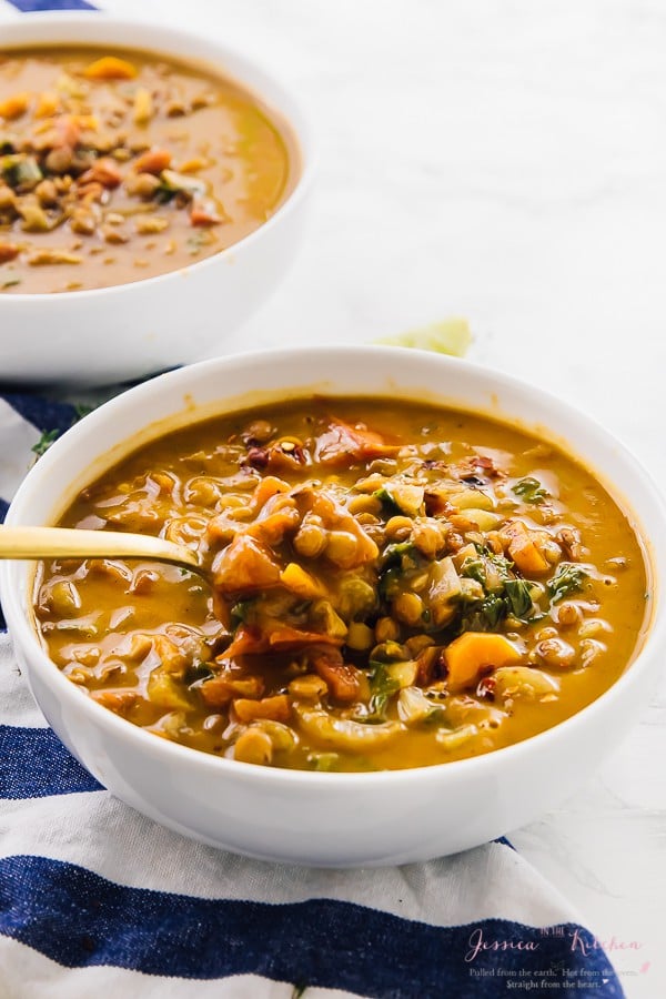 A spoon scooping into a white bowl of lentil soup. 